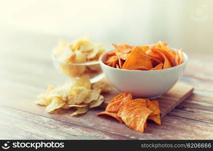 fast food, junk-food, cuisine and unhealthy eating concept - close up of crunchy potato crisps and corn crisps or nachos in bowls