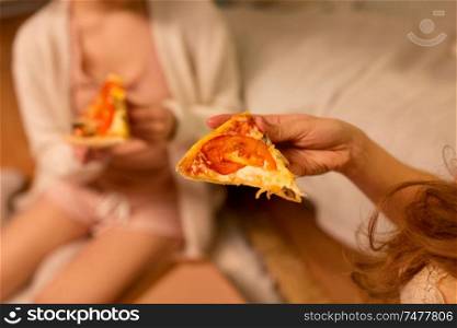fast food, pajama party and people concept - happy female friends eating pizza at home. happy female friends eating pizza at home