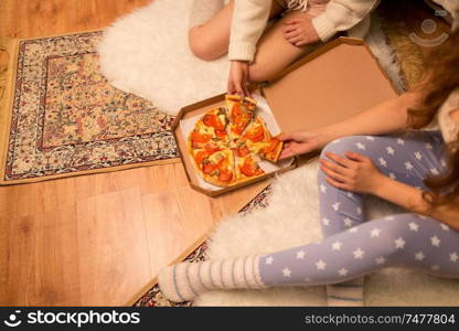 fast food, pajama party and people concept - happy female friends eating takeaway pizza at home. happy female friends eating pizza at home