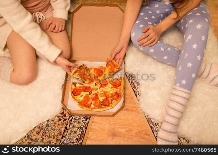 fast food, pajama party and people concept - happy female friends eating takeaway pizza at home. happy female friends eating pizza at home