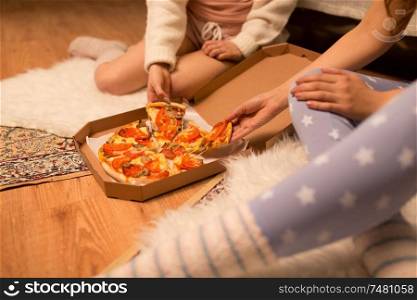 fast food, pajama party and people concept - happy female friends eating takeaway pizza at home. happy female friends eating pizza at home