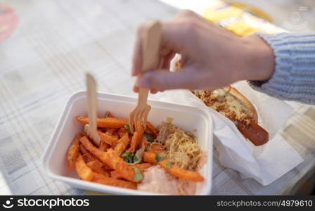 fast food, people and unhealthy eating concept - close up of hand with hot dog and sweet potato in disposable plate outdoors. close up of hand with hot dog and sweet potato