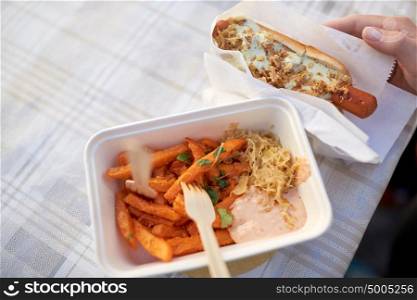 fast food, people and unhealthy eating concept - close up of hand with hot dog and sweet potato in disposable plate outdoors. close up of hand with hot dog and sweet potato