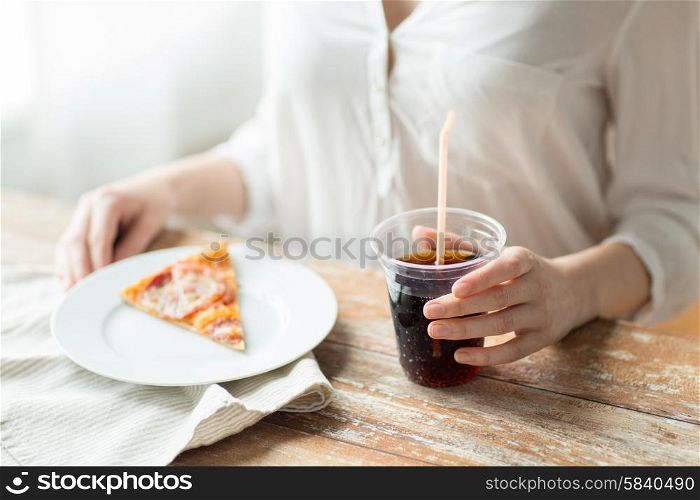 fast food, people and unhealthy eating concept - close up of woman hands with pizza and coca cola drink sitting at table