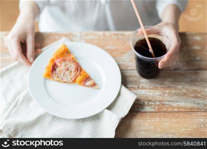 fast food, people and unhealthy eating concept - close up of woman hands with pizza and coca cola drink sitting at table