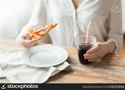fast food, people and unhealthy eating concept - close up of woman hands with pizza and cola drink sitting at table