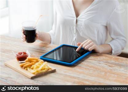 fast food, people, technology and diet concept - close up of woman with tablet pc computer eating french fries with ketchup, deep-fried squid rings and coca cola at wooden table