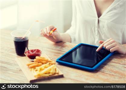 fast food, people, technology and diet concept - close up of woman with tablet pc computer eating french fries with ketchup, deep-fried squid rings and coca cola at wooden table