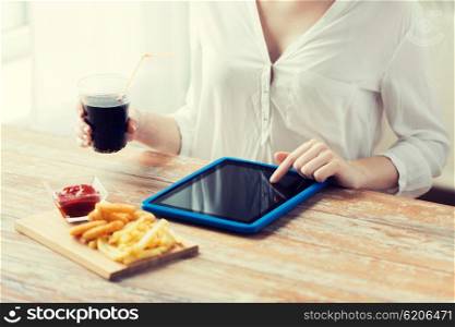 fast food, people, technology and diet concept - close up of woman with tablet pc computer eating french fries with ketchup, deep-fried squid rings and cola at wooden table
