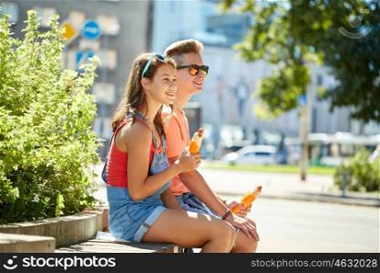fast food, summer and people concept - happy teenage couple eating hot dogs sitting on city street bench
