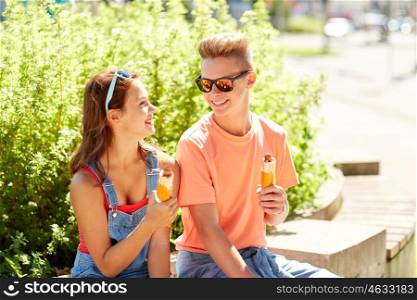 fast food, summer and people concept - happy teenage couple eating hot dogs sitting on city street bench