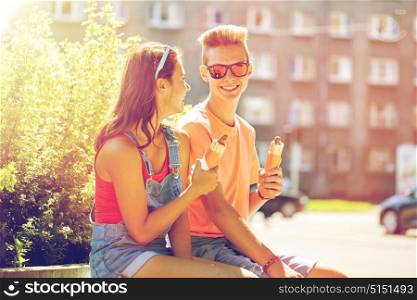 fast food, summer and people concept - happy teenage couple eating hot dogs sitting on city street bench. happy teenage couple eating hot dogs in city