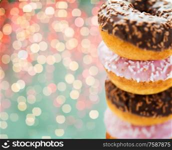 fast food, unhealthy eating and bakery concept - close up of glazed donuts with sprinkles over festive lights background. close up of glazed donuts with sprinkles