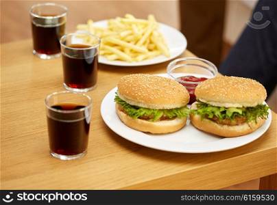 fast food, unhealthy eating and junk-food concept - close up of hamburgers, drinks and french fries on table at home