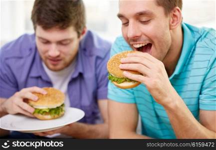 fast food, unhealthy eating, people and junk-food - close up of happy friends eating hamburgers at home