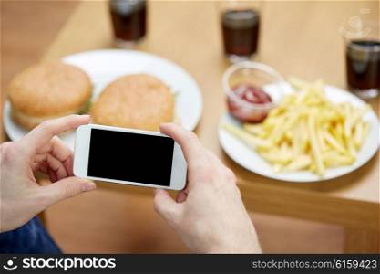 fast food, unhealthy eating, technology, people and junk-food - close up of man with smartphone photographing hamburgers and french fries at home