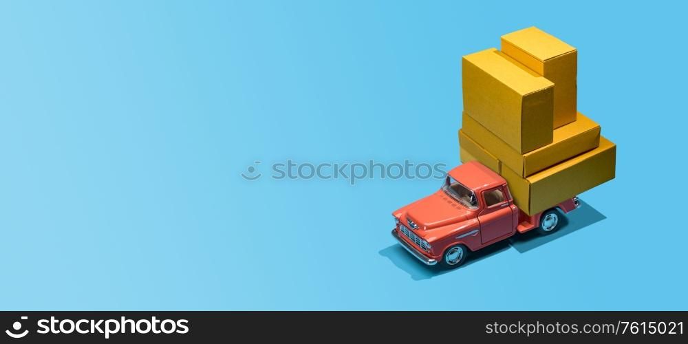 Fast order delivery by car concept. Pickup truck delivering blank boxes. Loaded retro toy car loaded with cardboard packages isolated on blue background.. Car delivering packages