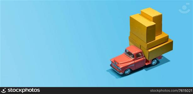 Fast order delivery by car concept. Pickup truck delivering blank boxes. Loaded retro toy car loaded with cardboard packages isolated on blue background.. Car delivering packages
