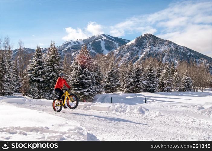 Fat bike (also called fat bike or fat-tire bike) - Cycling on large wheels. Teen rides a bicycle through the snow mountains in the background.