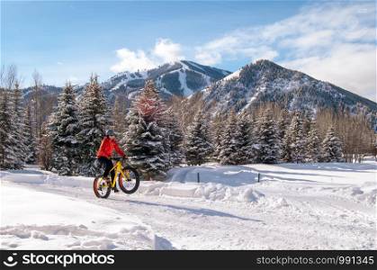 Fat bike (also called fat bike or fat-tire bike) - Cycling on large wheels. Teen rides a bicycle through the snow mountains in the background.