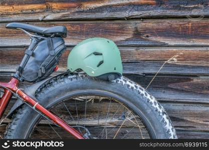 fat bike wheel , saddle and helmet against rustic wooden cabin wall