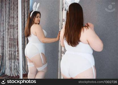 Fat depraved woman poses at the mirror in erotic bunny costume. Sexy overweight girl with big breast, perverse large size lady. Fat depraved woman poses at the mirror