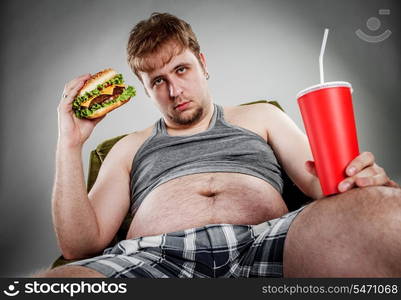 Fat man eating hamburger seated on armchair. Style fast food.