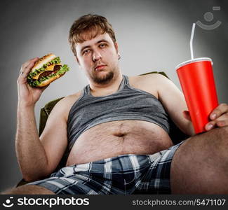 Fat man eating hamburger seated on armchair. Style fast food.