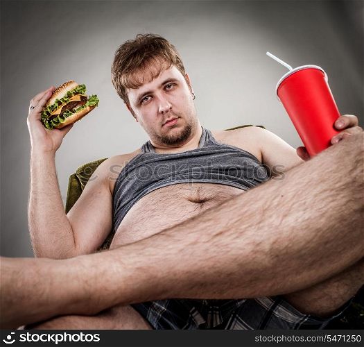 Fat man eating hamburger seated on armchair. Style fast food.