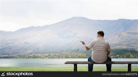 Fat man. Fat man sitting on bench with his back and pointing away with finger