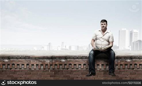Fat man. Fat man sitting on building top with book in hands