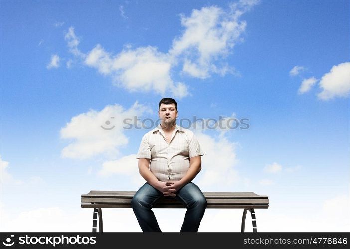 Fat man sitting on bench and looking away. Fat man