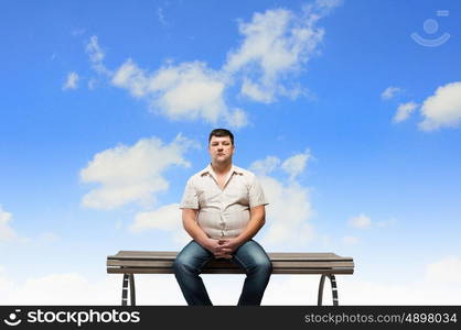 Fat man sitting on bench and looking away. Fat man