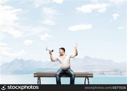 Fat man sitting on bench and screaming in megaphone. Fat man