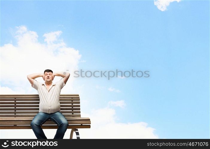 Fat man sitting on bench closing ears with hands. Fat man