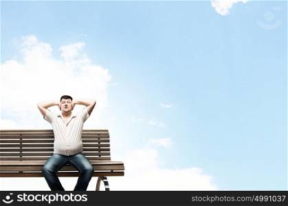 Fat man sitting on bench closing ears with hands. Fat man