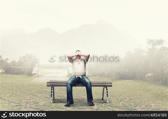 Fat man sitting on bench closing eyes with hands. Fat man