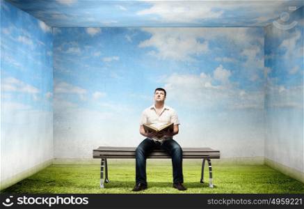Fat man sitting on bench with book and looking away. Fat man