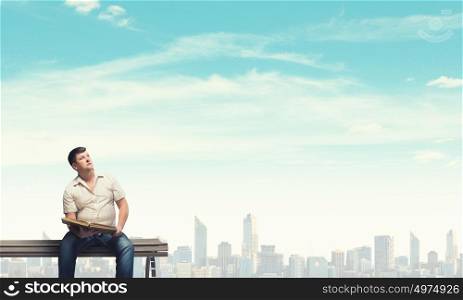 Fat man sitting on bench with book and looking away. Fat man