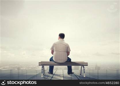 Fat man sitting on bench with his back and looking away. Fat man