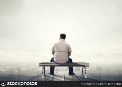 Fat man sitting on bench with his back and looking away. Fat man