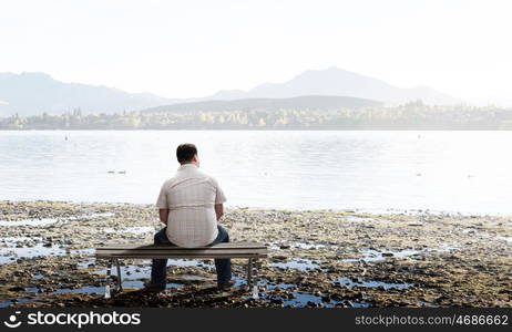 Fat man sitting on bench with his back and looking away. Fat man