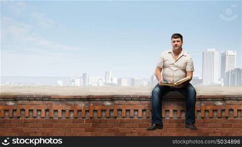 Fat man sitting on building top with book. Fat man