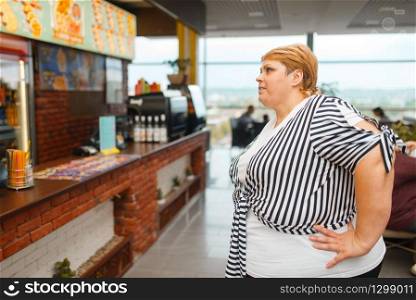 Fat woman at the fast food restaurant menu. Overweight female person buying fastfood, obesity problem. Fat woman at the fast food restaurant menu