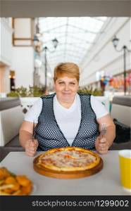 Fat woman eating pizza in fastfood restaurant. Overweight female person at the table with junk dinner, obesity problem. Fat woman eating pizza in fastfood restaurant