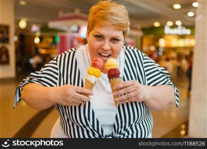 Fat woman eating two ice creams in fastfood mall restaurant. Overweight female person with ice-cream, obesity problem