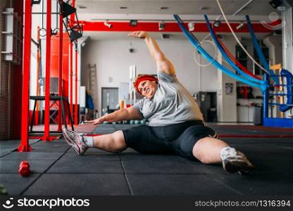 Fat woman exercises on the floor, workout in gym. Calories burning, obese female person, training in sport club. Fat woman exercises on the floor, workout in gym