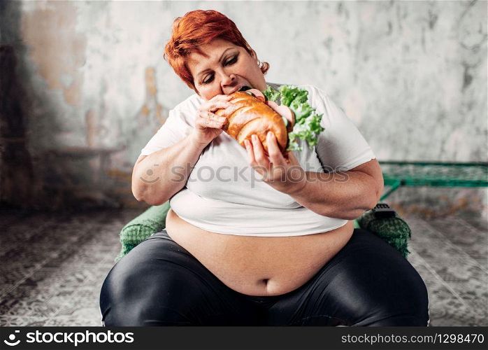 Fat woman sits in a chair and eats sandwich, bulimic and overweight. Unhealthy lifestyle, obesity. Fat woman sits in chair and eats sandwich, bulimic