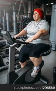 Fat woman training on exercise bike in gym. Calories burning, obese female person in sport club. Fat woman training on exercise bike in gym