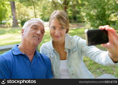 father and adult daughter taking selfie in the parc